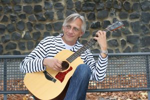 Christian Straube sitzt auf einer Bank und spielt Gitarre