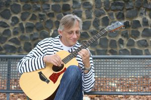 Christian Straube sitzt auf einer Bank und spielt Gitarre
