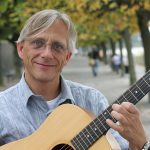 Christian Straube mit Gitarre und der der Beueler RHeinpromenade in Hintegrund