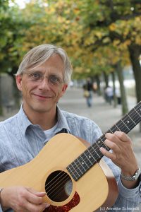 Christian Straube mit Gitarre und der der Beueler RHeinpromenade in Hintegrund