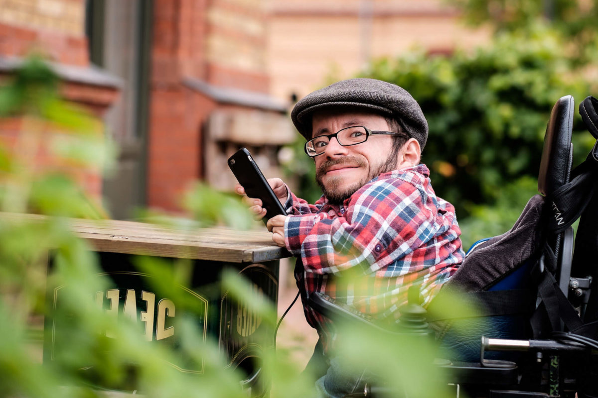 Raul Krauthausen mit Handy in Biergarten