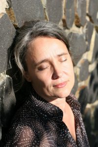 Sabria im Sonnenlicht an Steinmauer gelehnt