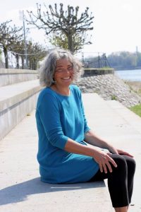 Christine sitzt auf den Treppen am Rhein und lacht in die Kamera