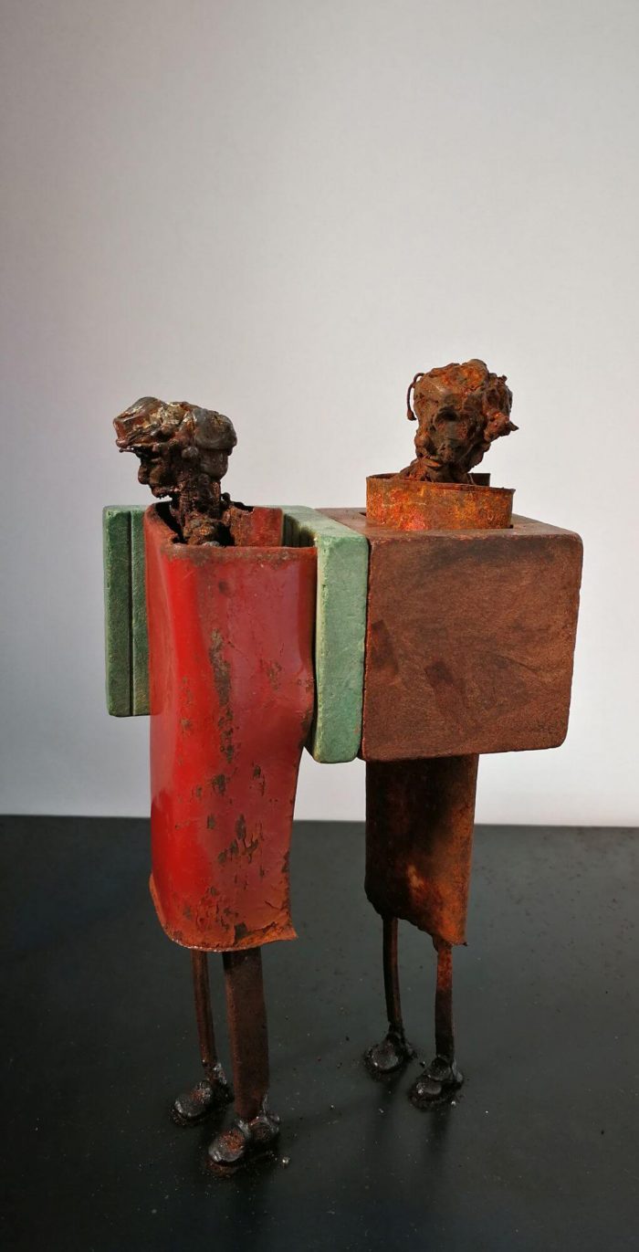 Two metal figures behind each other, one caught in a block sucking the one in front of him in.