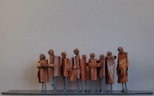 Eight metal figures standing in line behind each other looking like they'd hold each other by the waist and one bigger figure at the end oerseeing them.