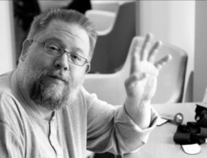 Bärtiger Mann mit Brille winkt in die Kamera