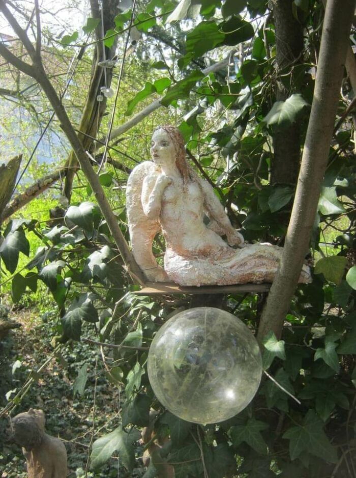 Im Baum sitzende Frauenskulptur über einer gläsernen Blase