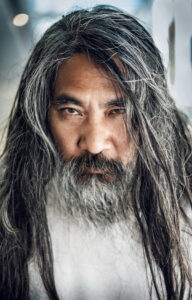 Man with long dark hair and beard, starting to get grey