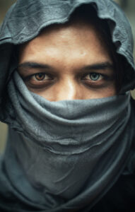 Man with a blue and an brown eye wearing a headscarf hiding his mouth and lower nose
