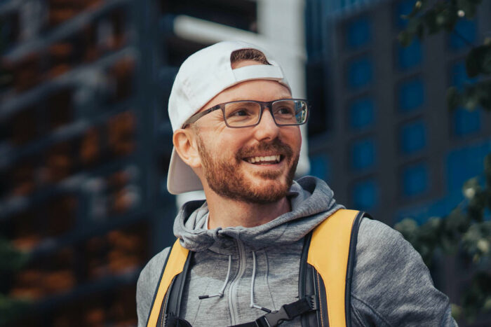 Dino lachend mit weißer Baseballkappe, Brille, rothaarigem Bart