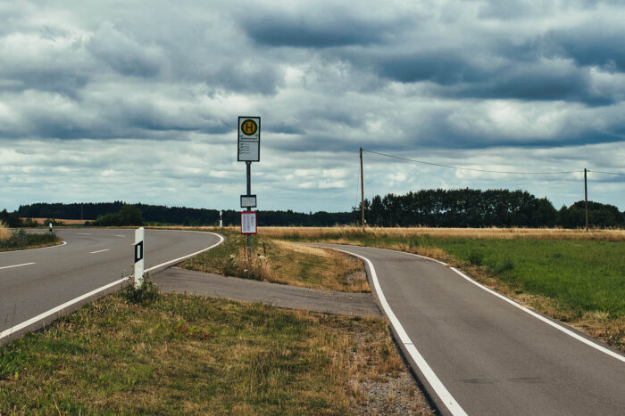 Bushaltestellen-Schild im Nirgendwo mit schwerem Wolkenhimmel zwischen einsamer Landstaße und Fahrradweg