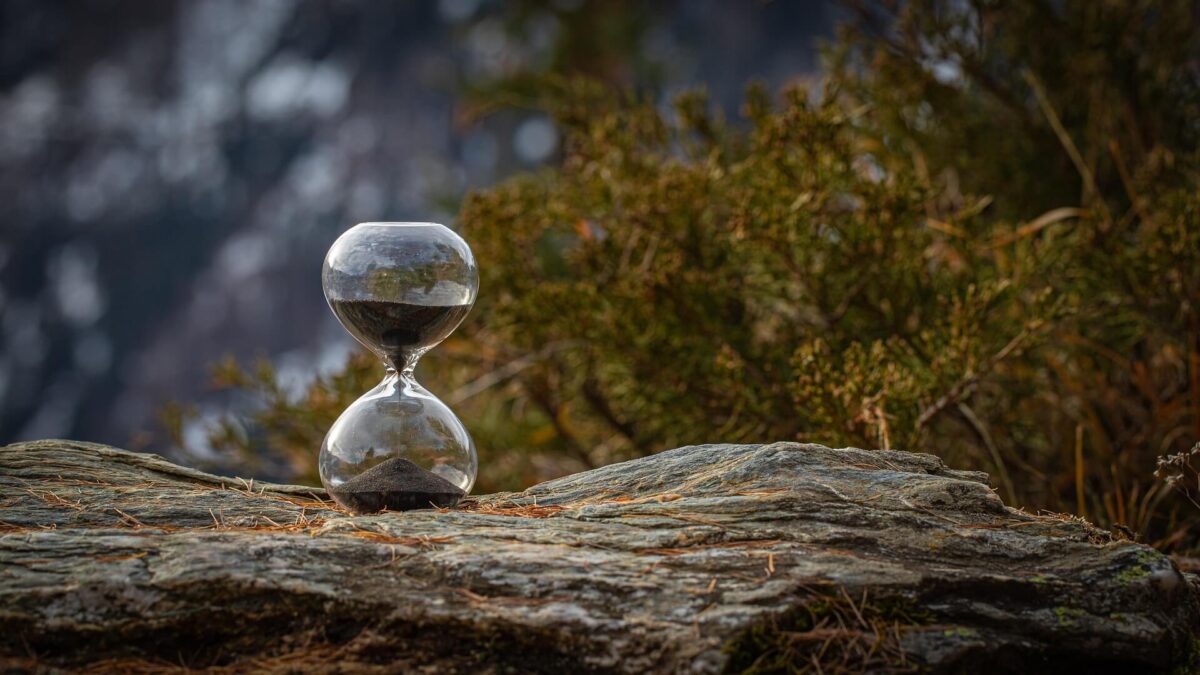 Sanduhr auf einem Felsen mit Wald und Gebirge im Jintergrund