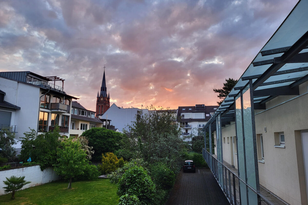 Blick über Hinterhofgärtrn in Bonn Beuel bei Sonnenaufgang. Große dunkle Wolken am Himmel, pink leuchtener Horizont.