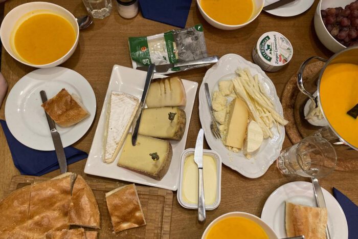 Tisch voller Suppenschalen, Gläser, und Käseteller mit Trauben, daneben ein Fladenbrot