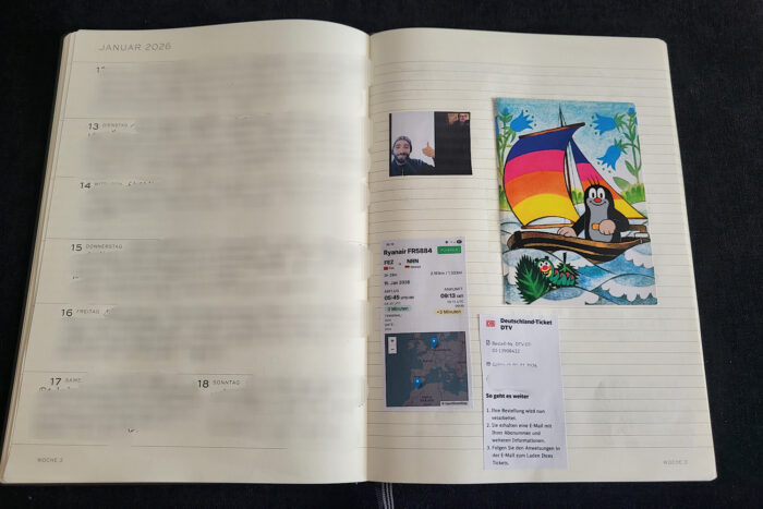 Aufgeklapptes Kalenderbuch mit verwischter Schrift links und eingeklebten Schnipseln von Thamis Flug nach Deutschland und einer Maulwufpostkarte