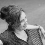 Sabria lächelnd auf einer Bank mit Blick in die Ferne