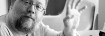 Bärtiger Mann mit Brille winkt in die Kamera